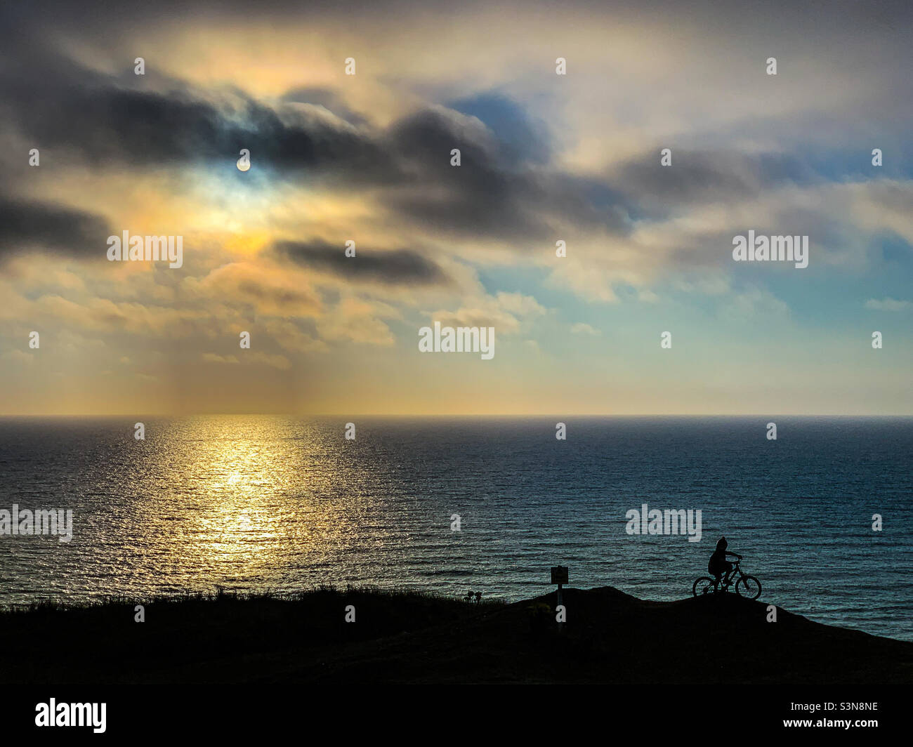 Child cycling silhouette in front of sea in Cornwall at dusk - Smartphone Captured Stock Image