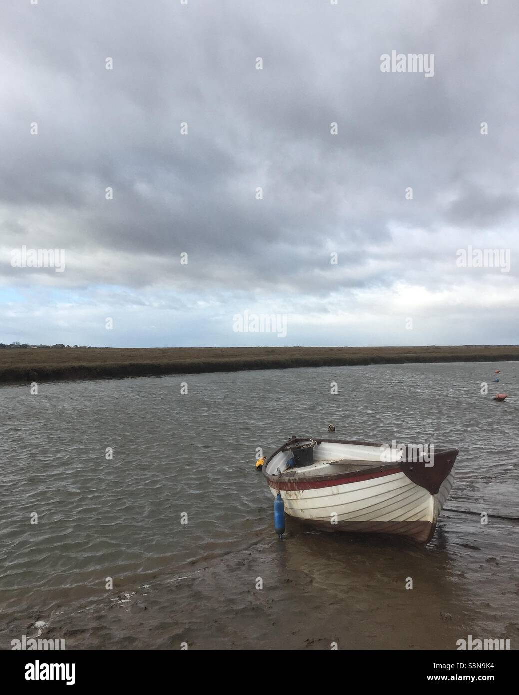 A small rowing boat moored beside a tidal creek on the Blakeney marshes in Norfolk, England. - Smartphone Captured Stock Image