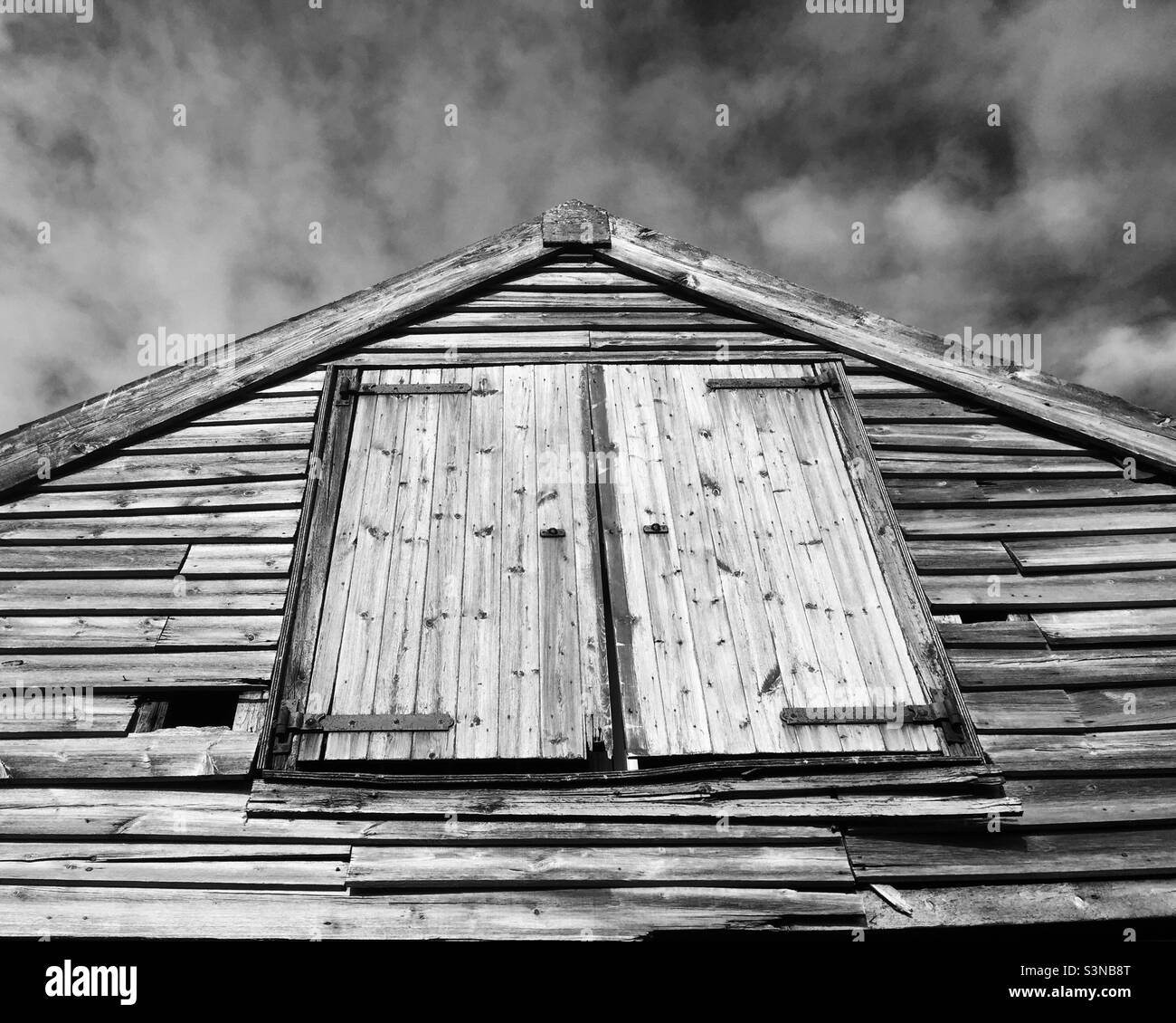 Abstract view of an old wooden building at Thornham, Norfolk against a cloudy sky. The image had been converted to black and white. - Smartphone Captured Stock Image