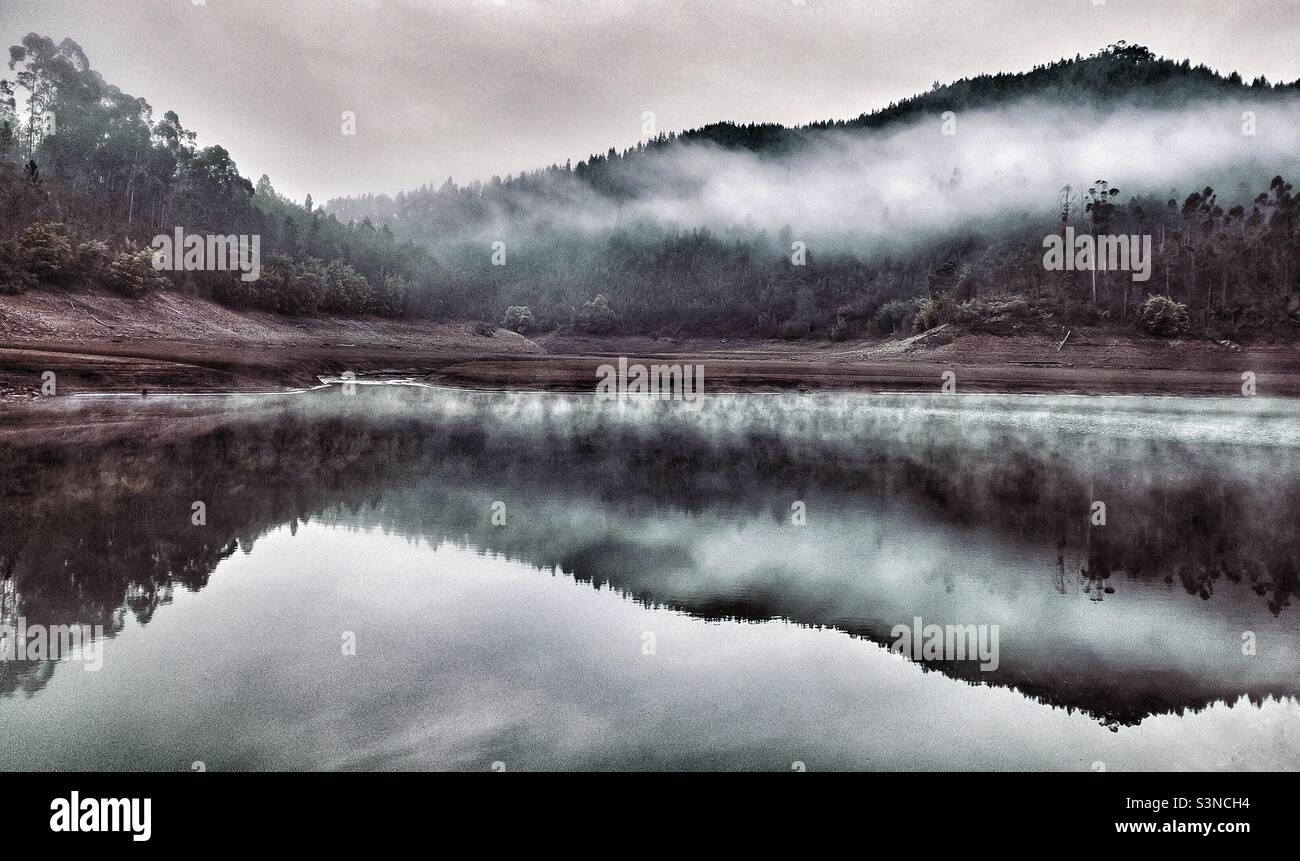 Early morning mist hangs over the tree lined hills and is reflected in the river - Smartphone Captured Stock Image