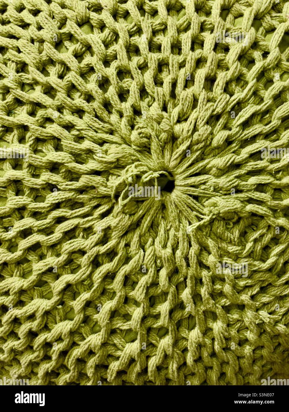 A close-up of a knitted pouffe, showing a radial pattern of stitches in a thick green wool - Smartphone Captured Stock Image