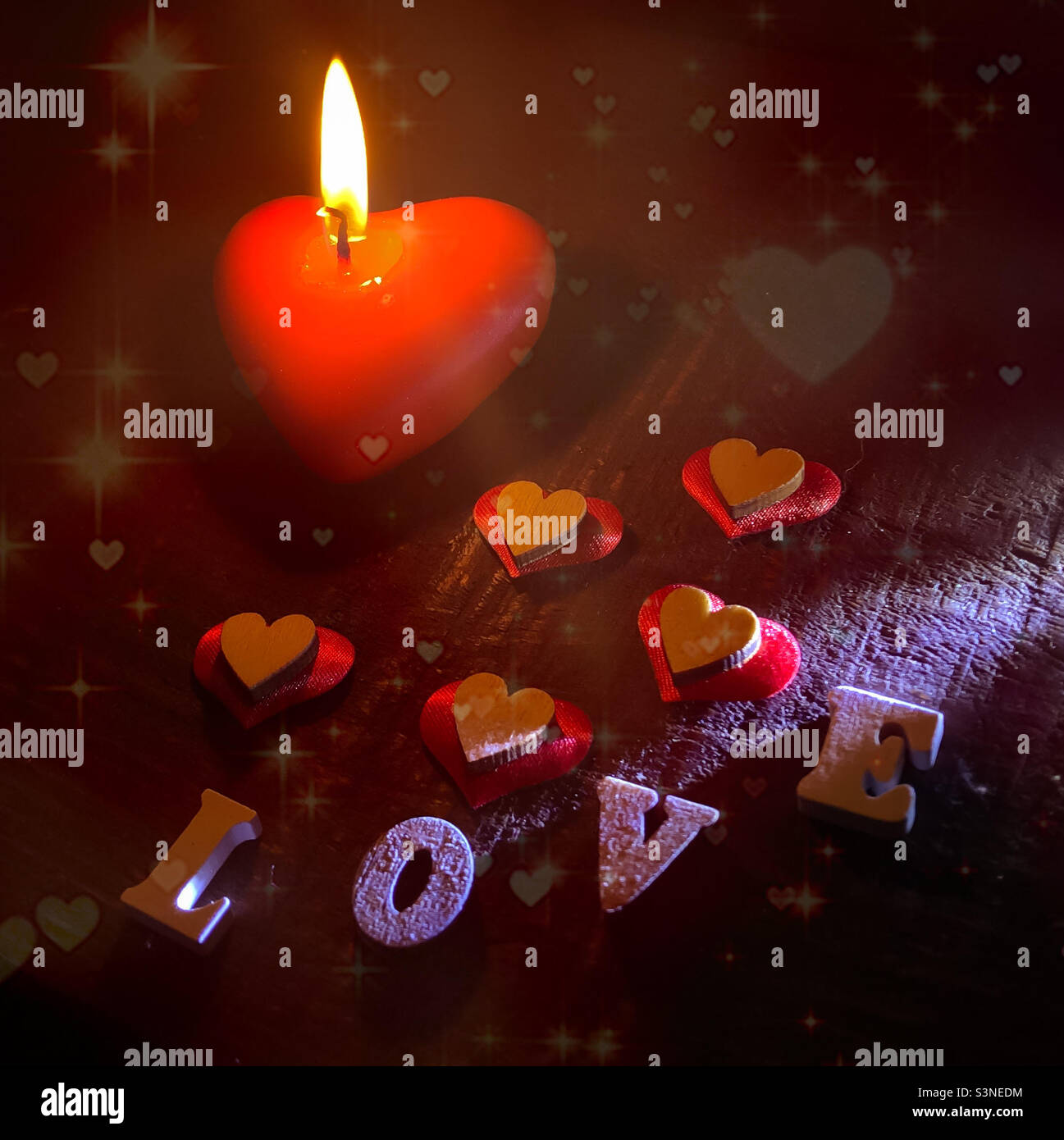 A lit, red, heart shaped candle with wooden hearts on cushions on read and the word Love spelled out - Smartphone Captured Stock Image