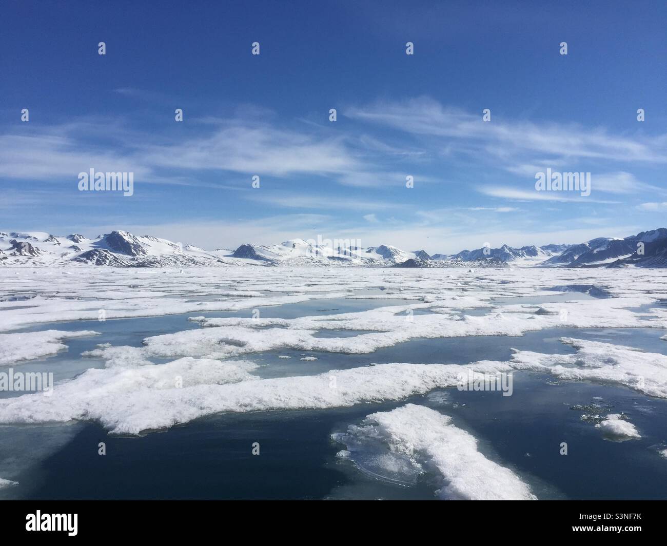 Fractured sea ice and snow capped mountains in Svalbard under a blue sky with broken white clouds - Smartphone Captured Stock Image