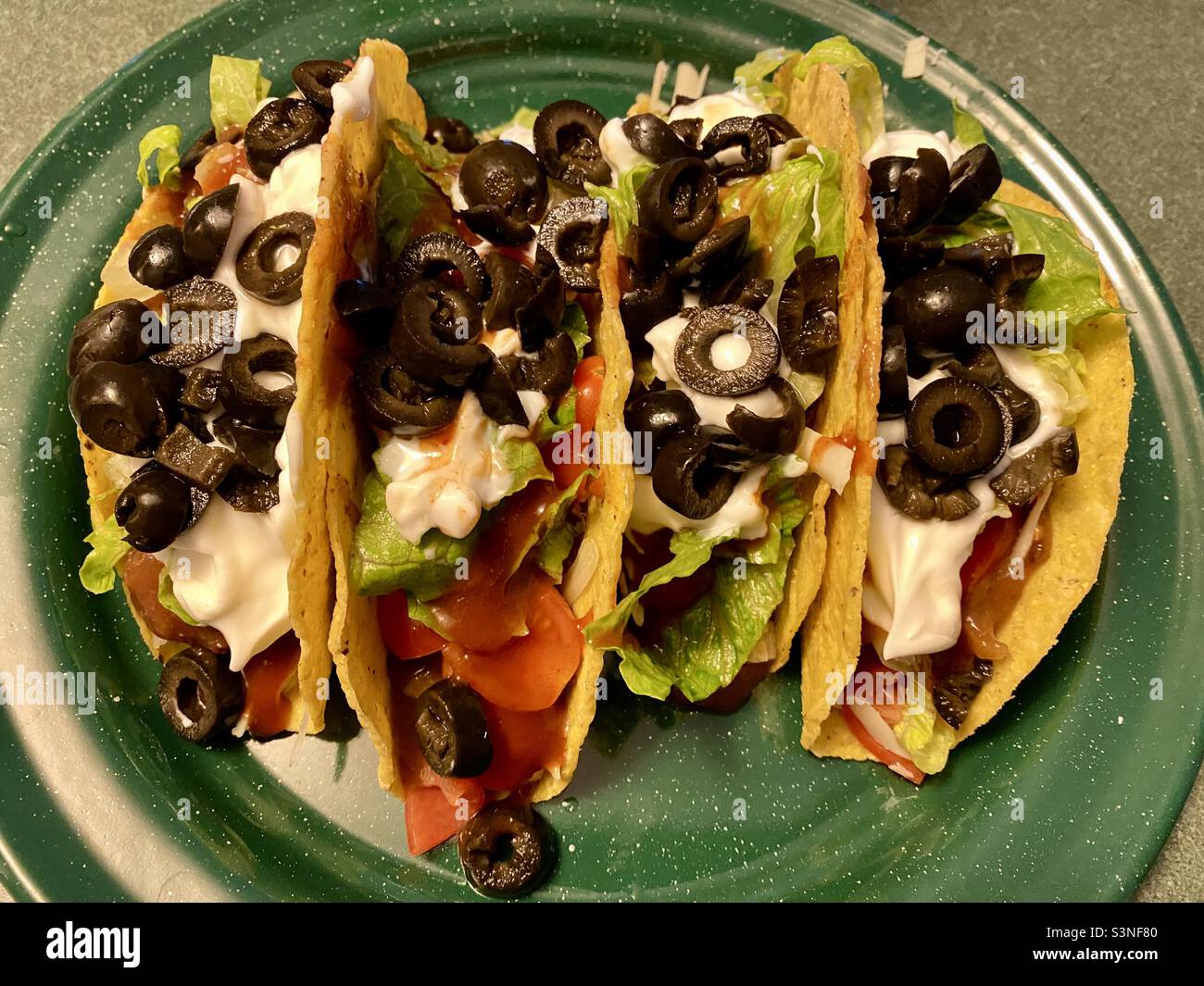 4 taco shells on a green plate filled chicken, cheese, salsa, tomatoes