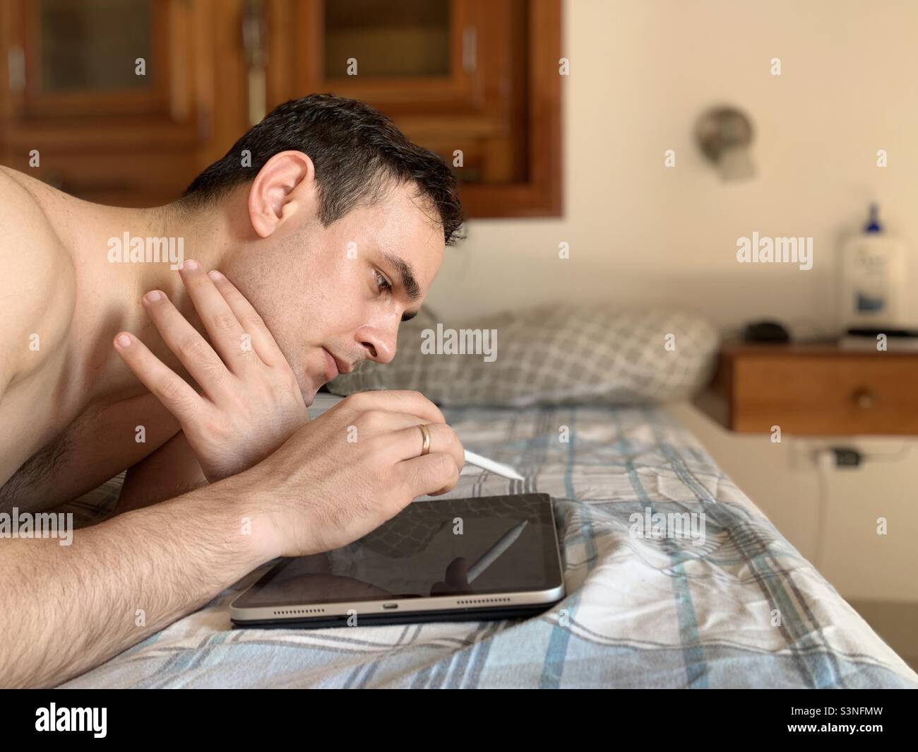 Designer working on iPad lying on bed with early morning sunlight. Creative work. - Smartphone Captured Stock Image
