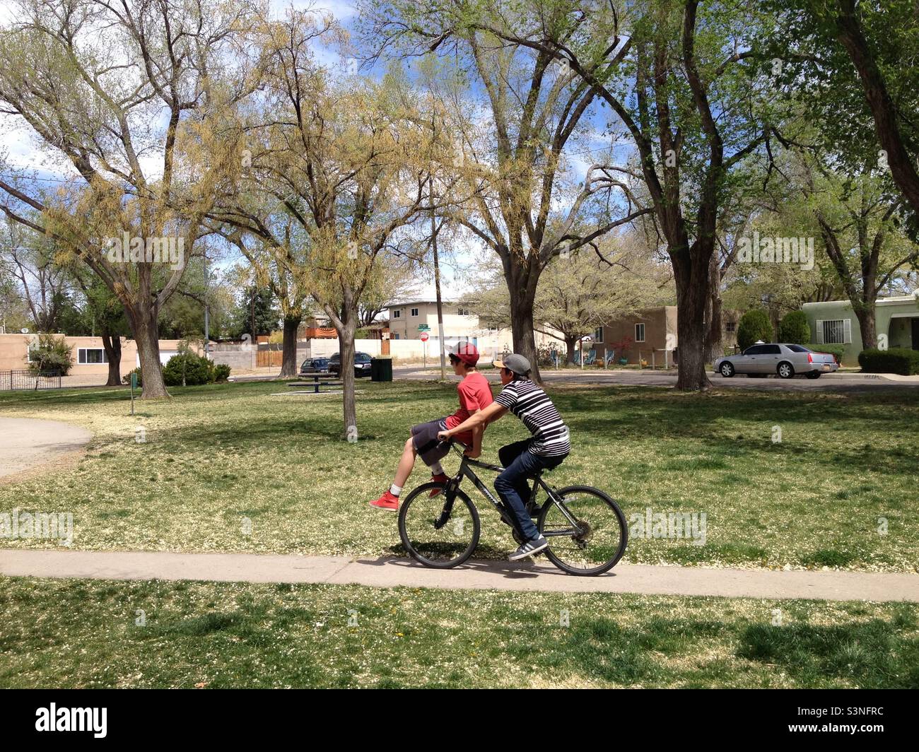 Two middle school age boys ride on a bike in United States, public park, Springtime. Stock Photo