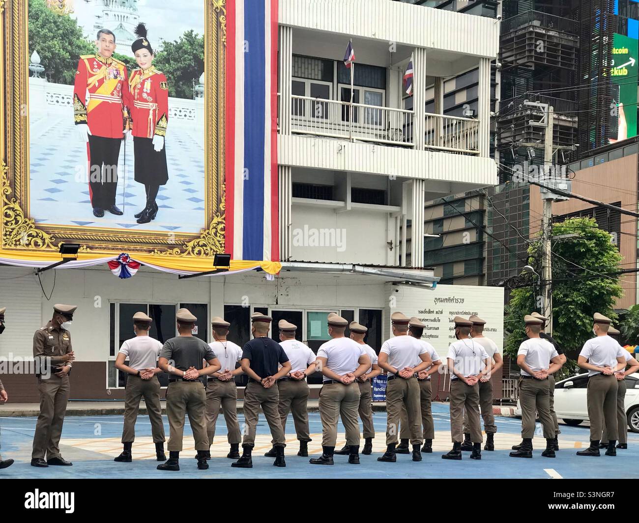 Thailand police stand to attention and line up in front of a large poster image of the Thailand King and Queen. Thailand, Southeast Asia - Smartphone Captured Stock Image