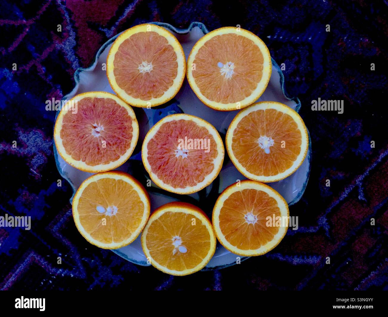 Fresh-Cut, juicy oranges, arranged in a circle. Full of vitamin C. Dark, oriental rug as a backdrop. Eight halves. - Smartphone Captured Stock Image
