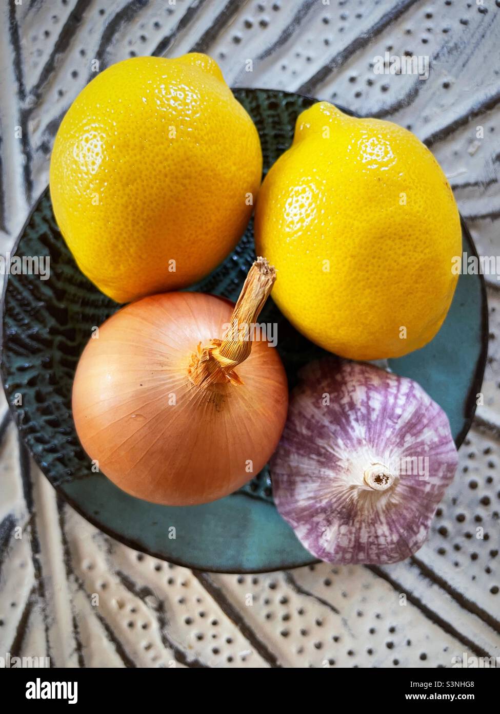Still life of lemons, onion and garlic bulb on a pottery plate - Smartphone Captured Stock Image