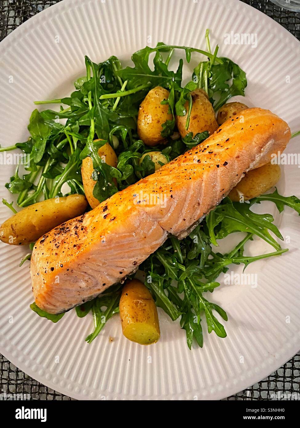 Flat layer of a gourmet one dish seafood meal of broiled salmon on a bed of arugula and tiny potatoes, 2022, USA - Smartphone Captured Stock Image
