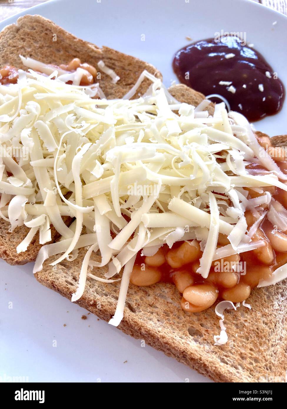 Beans on toast with grated cheddar cheese and brown sauce Stock Photo