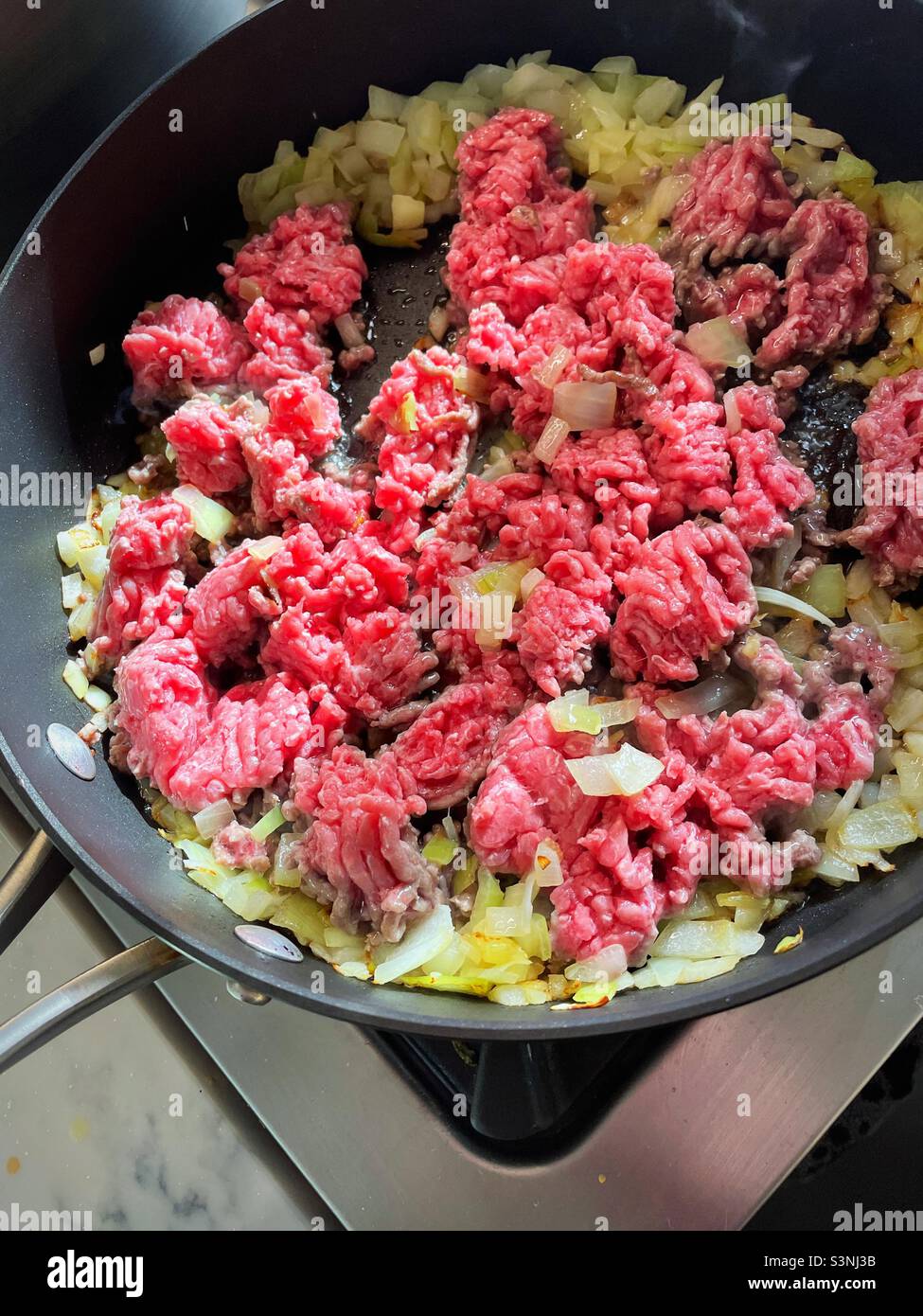 Close up of raw ground beef being fried in a skillet on a residential stove top, 2022, USA - Smartphone Captured Stock Image