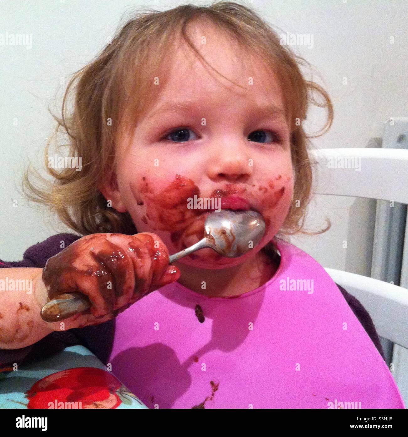 Young girl, gets covered in chocolate, while eating it with a spoon Stock Photo