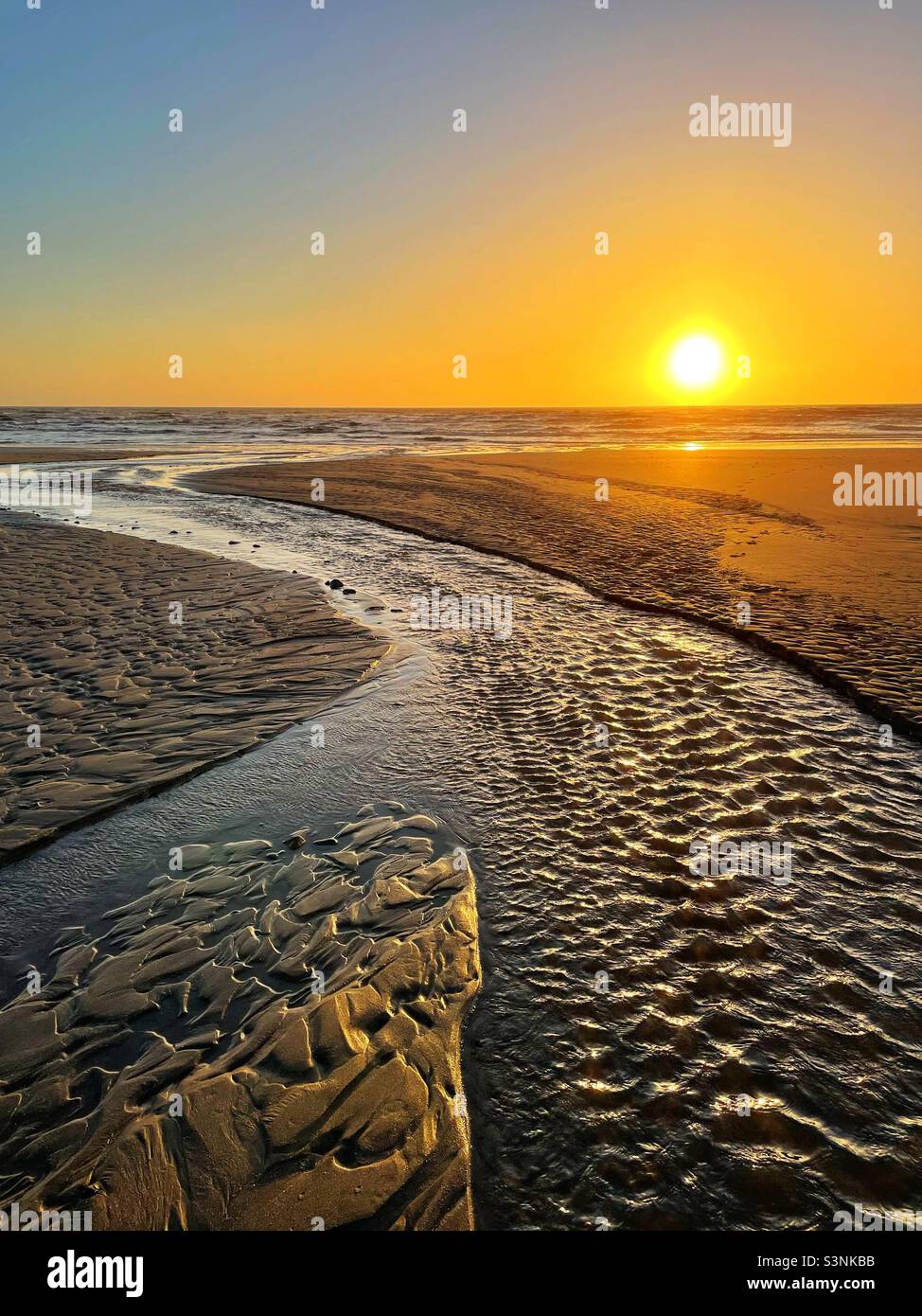 Sunset over the ocean with a stream reaching the sea. Stock Photo