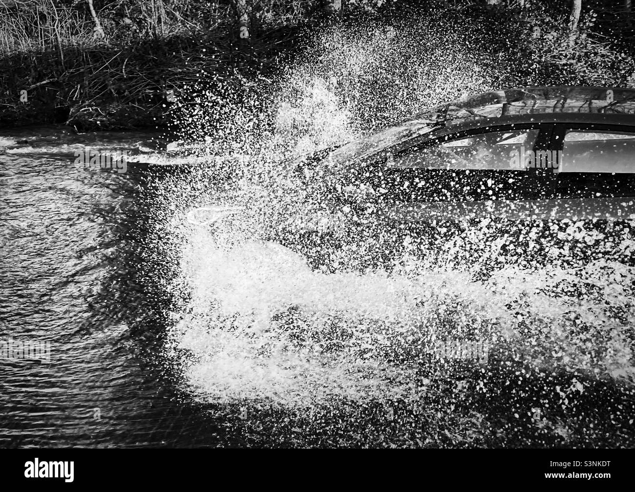 ‘Going for it!’ A motorists decides that they are putting their foot to the floor and driving through the flooded road ahead (Black & White) Stock Photo
