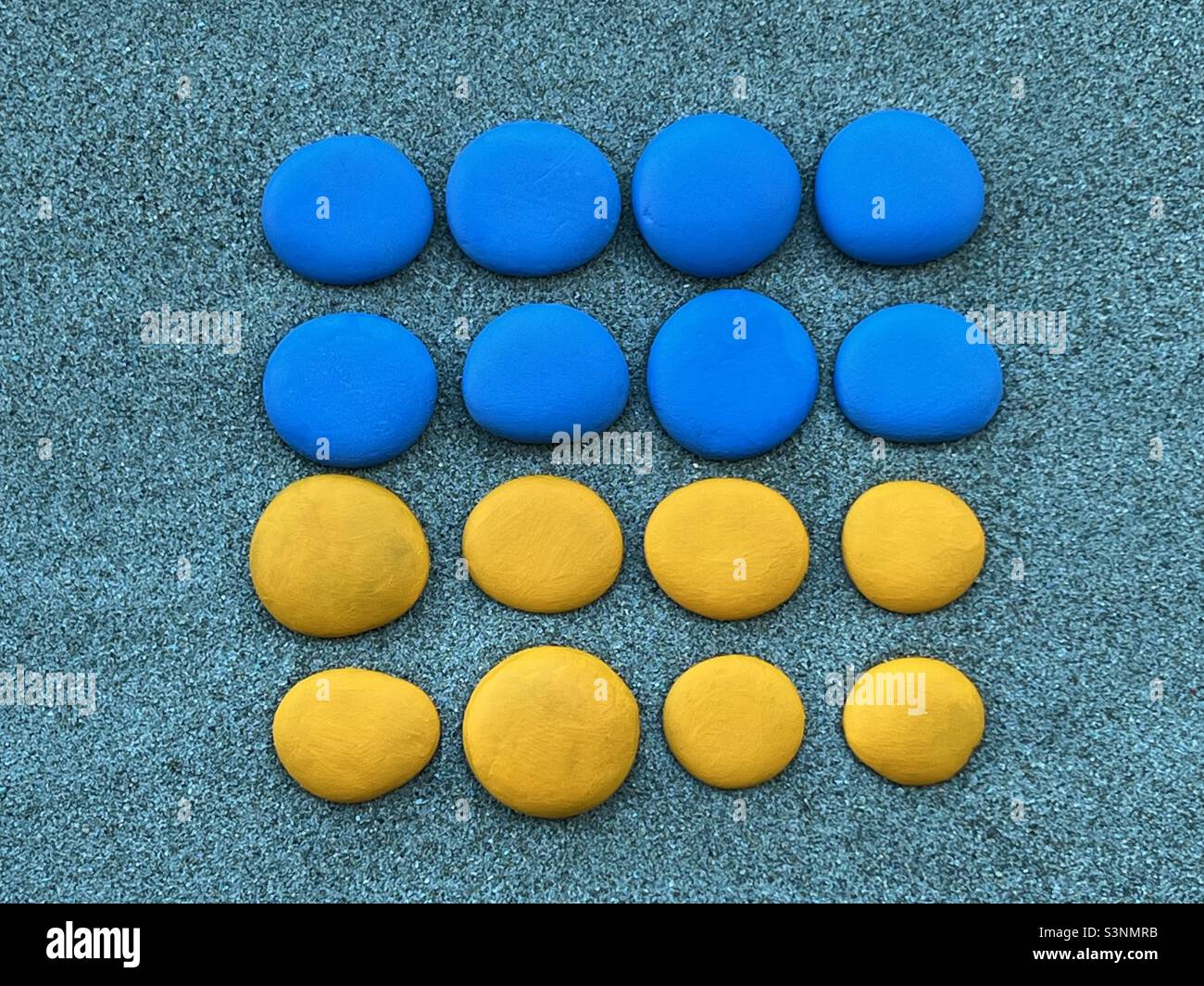 The national flag of Ukraine composed with blue and yellow hand painted pebbles over green sand - Smartphone Captured Stock Image