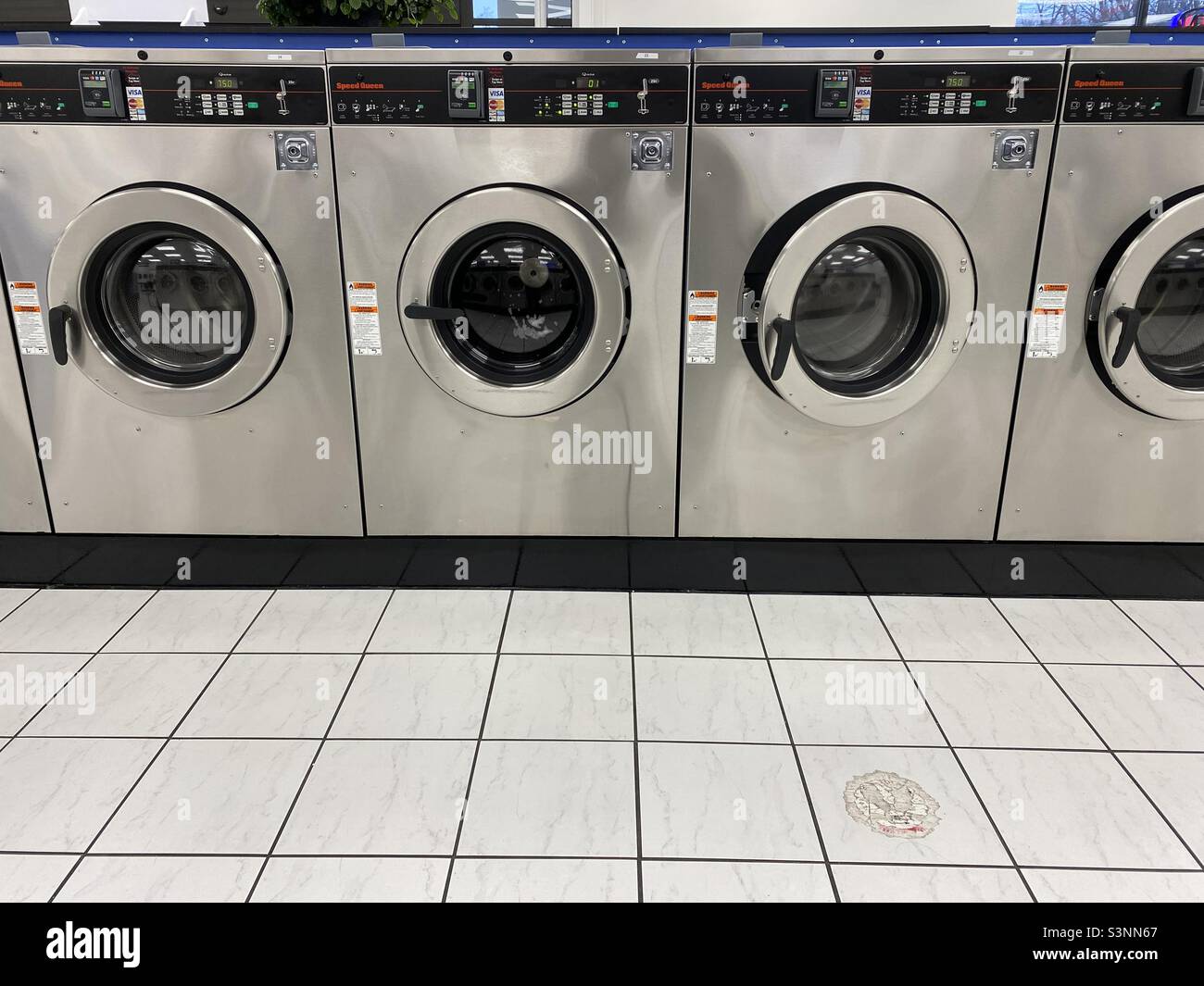 Stainless steel washing machines sit idle in an empty laundromat. Stock Photo