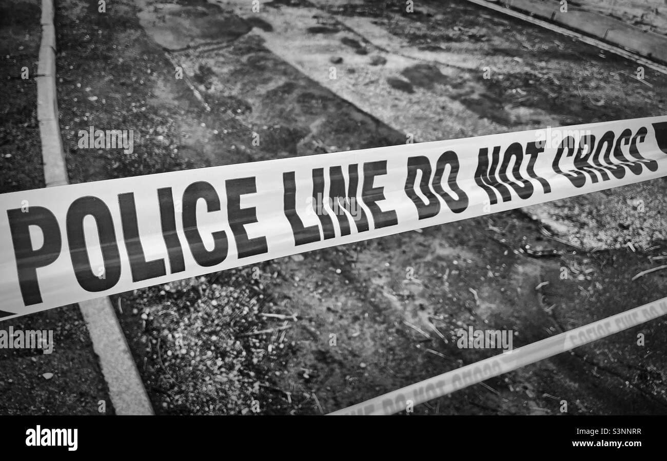 ‘Crime Scene Investigation’ a do not cross Police Line is taped across a road to keep the public away from a crime scene (Black & White) Stock Photo