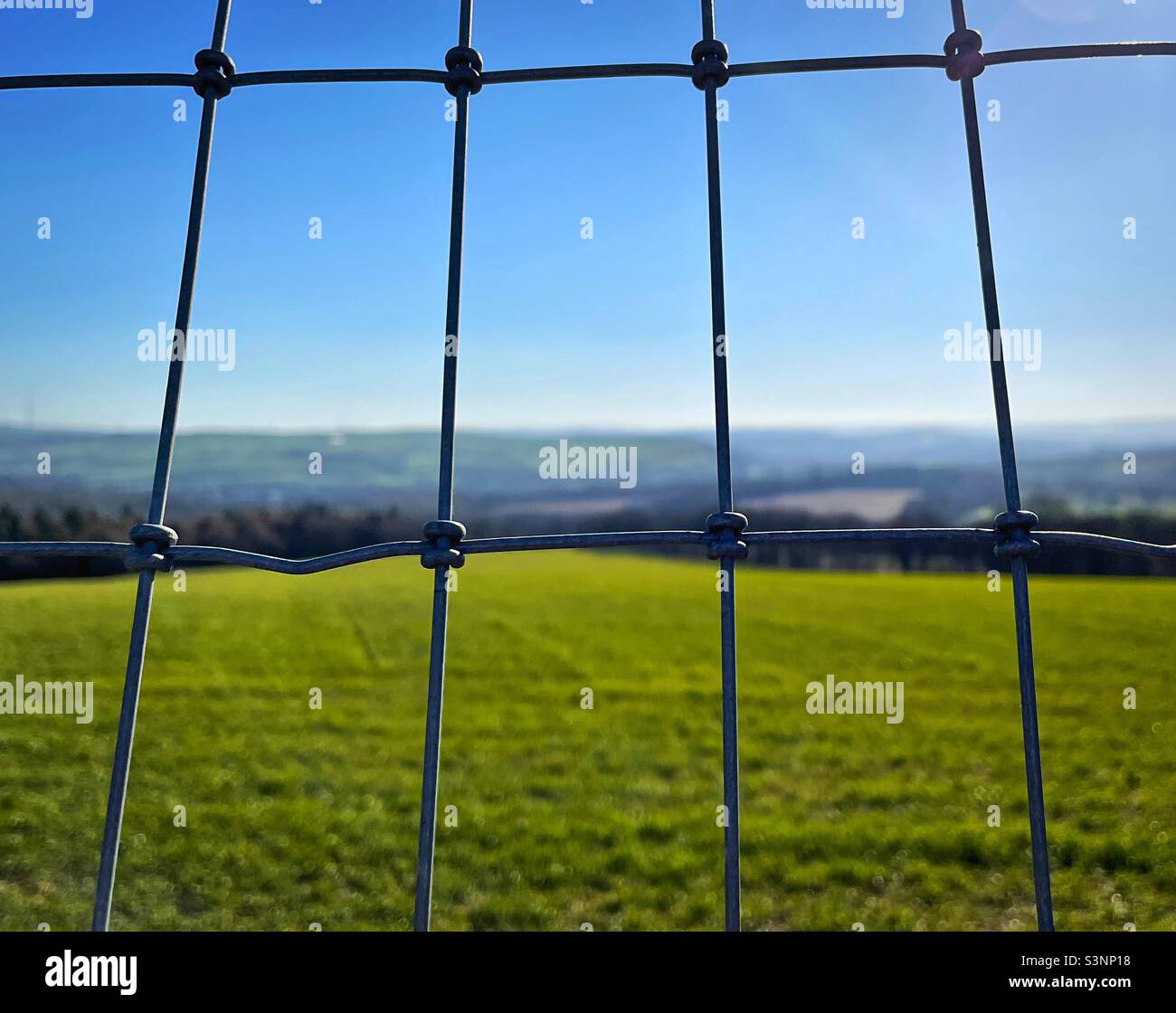 ‘Spoiling the view’ a metal wire fence blurs the view of the stunning countryside landscape on a clear blue sky day Stock Photo