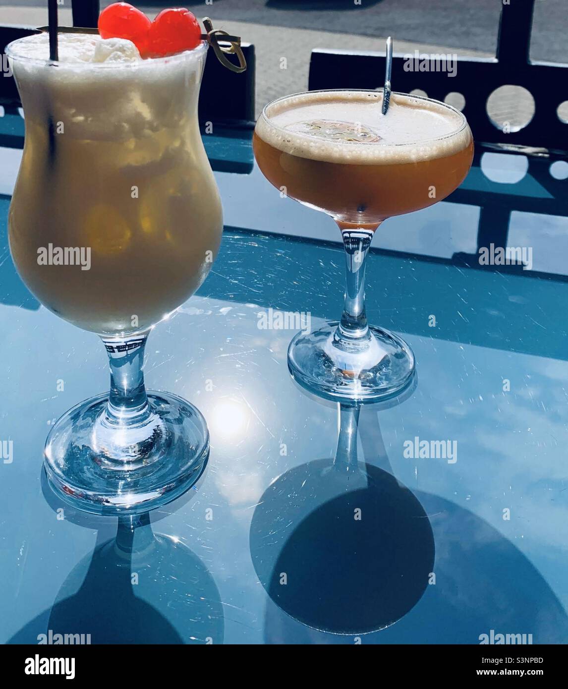 Cocktails Pina Colada and Pornstar Martini reflecting on a glass table in the sunshine Stock