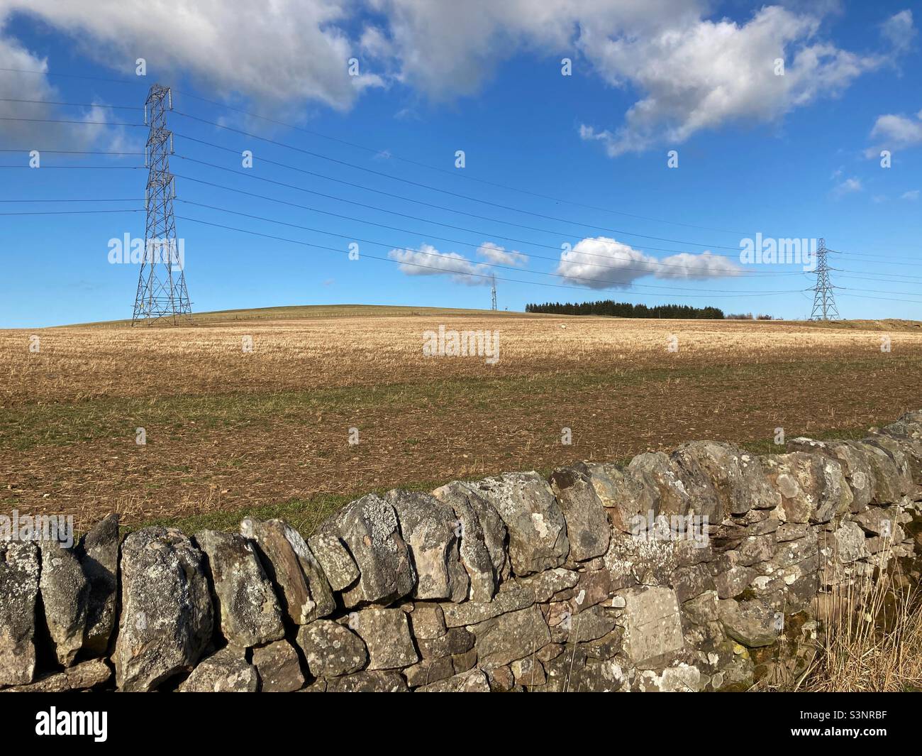 Electricity pylons in a ploughed field on a sunny day - Smartphone Captured Stock Image