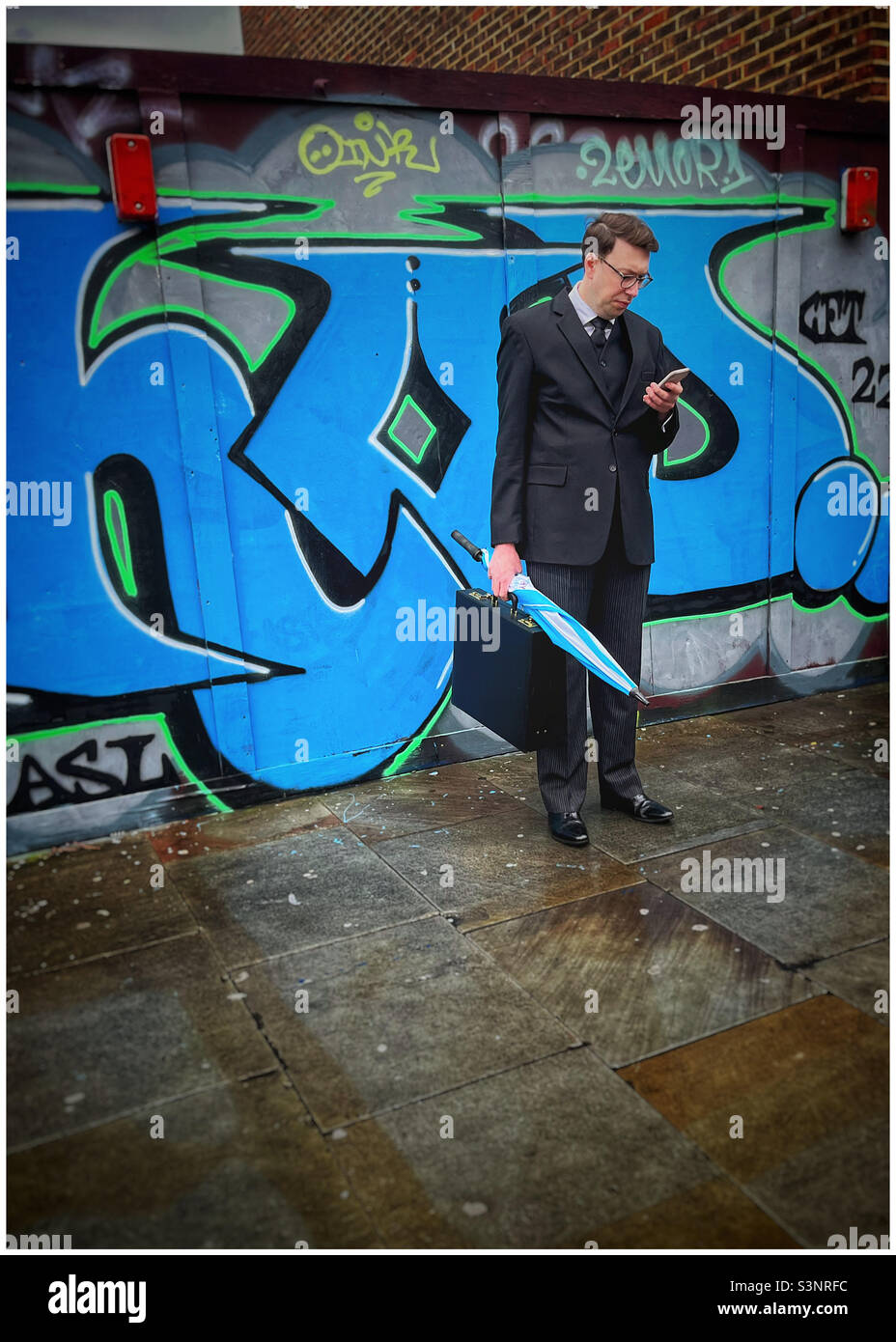 Businessman checking phone in front of street graffiti in Waterloo, London - Smartphone Captured Stock Image