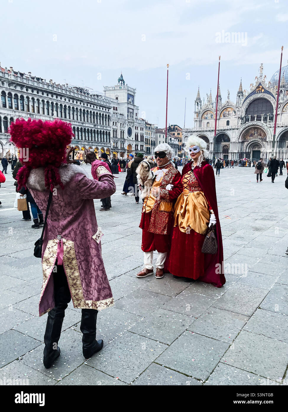 People dressed in historic costumes in St. Mark Square in Venice, Italy  during Carnevale. On man dressed in costume is taking a picture of a couple  also dressed up for the festivities