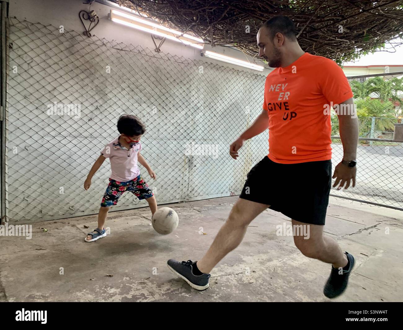 Father plays soccer with his son with a ‘never give up’ sign on his t-shirt. Fatherhood. Havana, Cuba, Latin America, Caribbean Stock Photo