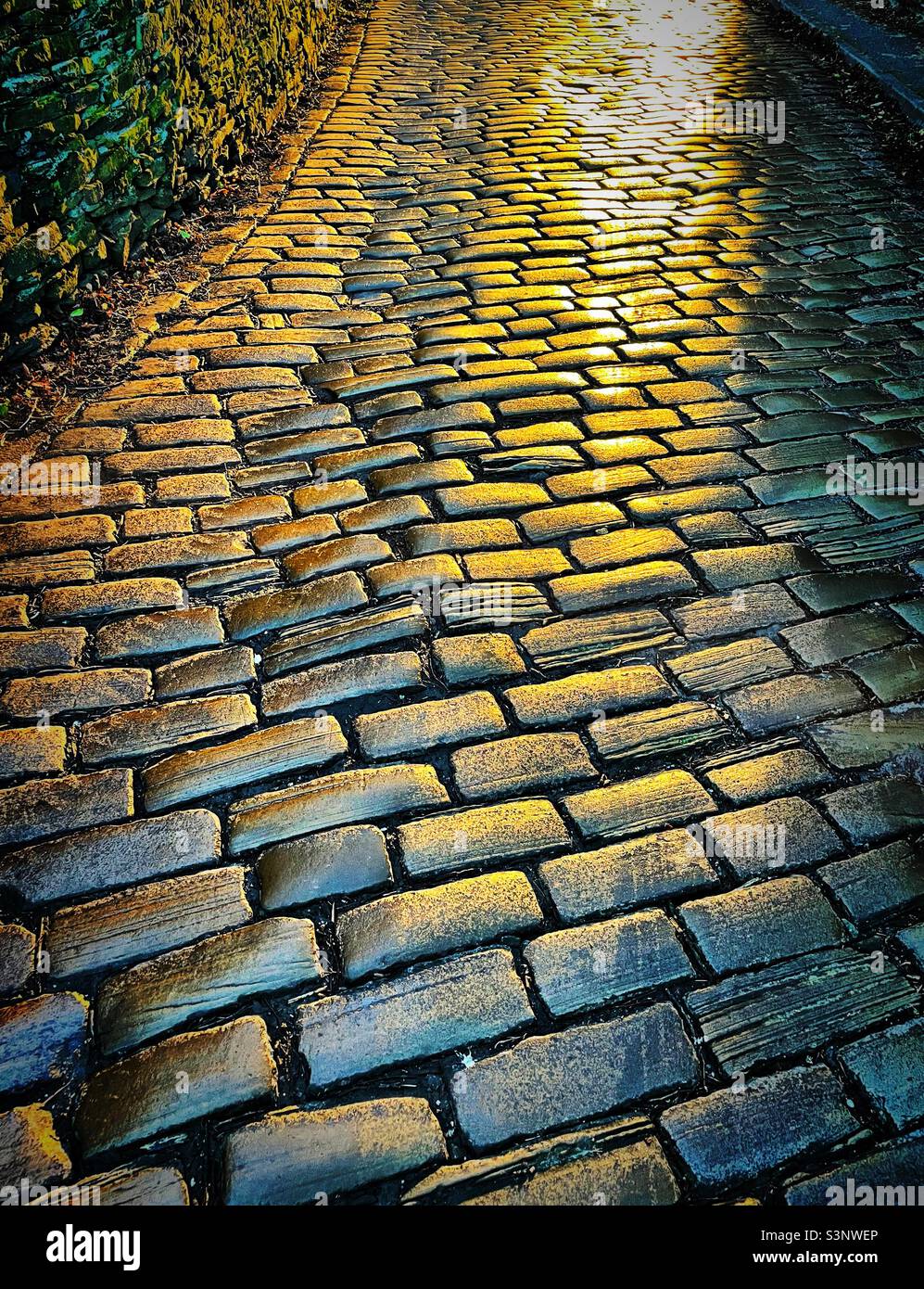 ‘Golden Cobbles’ the traditional old Yorkshire cobbles shine brightly with the reflection of evening sunset Stock Photo