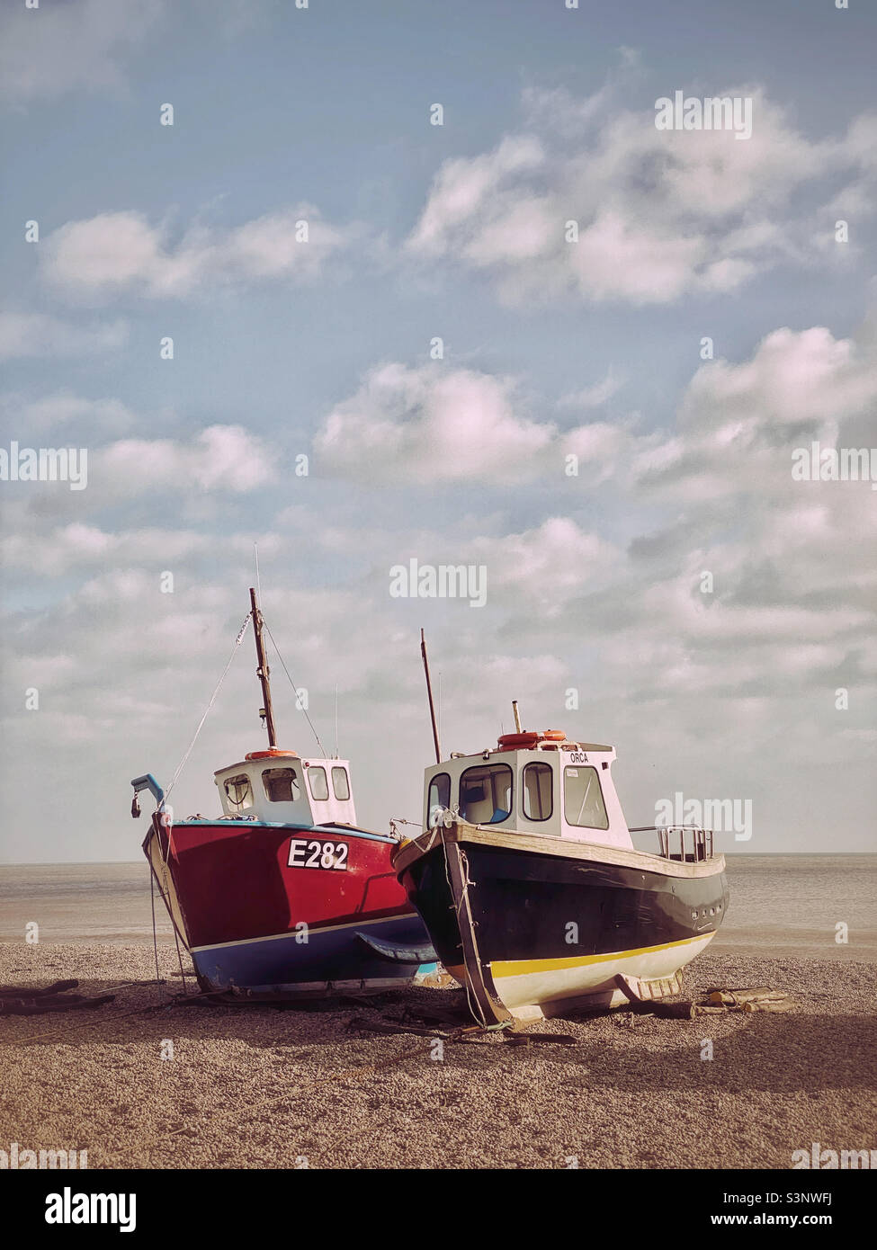 Two trawler boats atop a pebbly beach on the south coast of England. A slightly desaturated technique has been used to create an atmospheric effect. Photo ©️ COLIN HOSKINS. - Smartphone Captured Stock Image