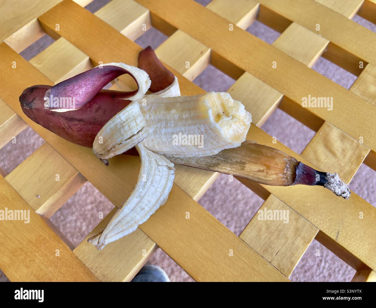 A half eaten red skinned banana resting on the gridded top of a birch wood coffee table - Smartphone Captured Stock Image