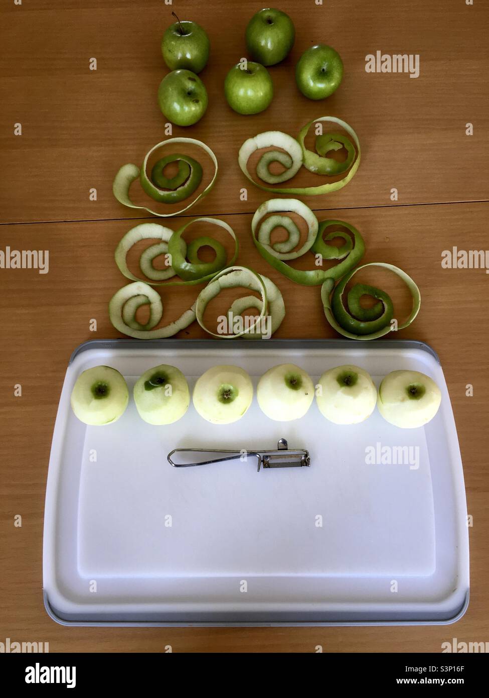 Green apples with peel and tool, on white board and brown wooden table - Smartphone Captured Stock Image