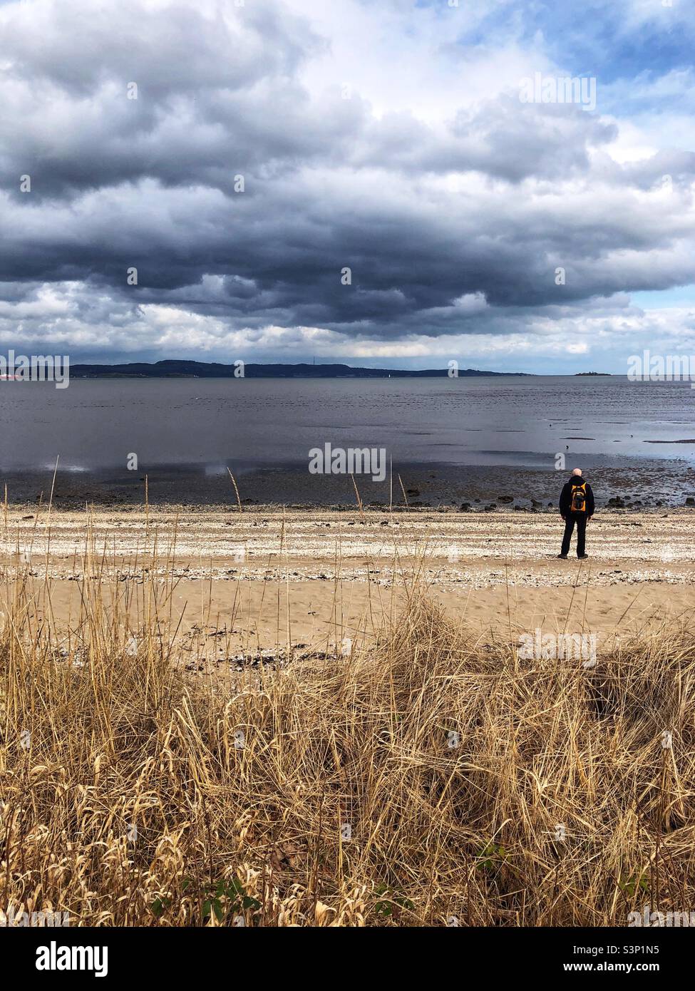 Man standing on the beach looking out to the estuary under a brooding sky - Smartphone Captured Stock Image
