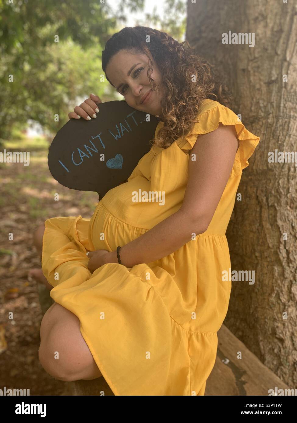 Pregnant woman holds an ‘I can’t wait’ text looking happily at the camera. Pregnancy concept. Havana, Cuba, Latin America. - Smartphone Captured Stock Image