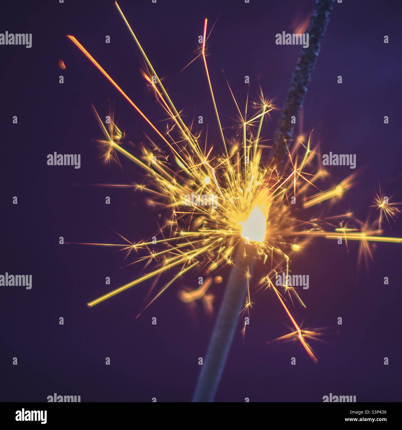 Close up of a sparkler burning brightly in contrast with a purple background - Smartphone Captured Stock Image