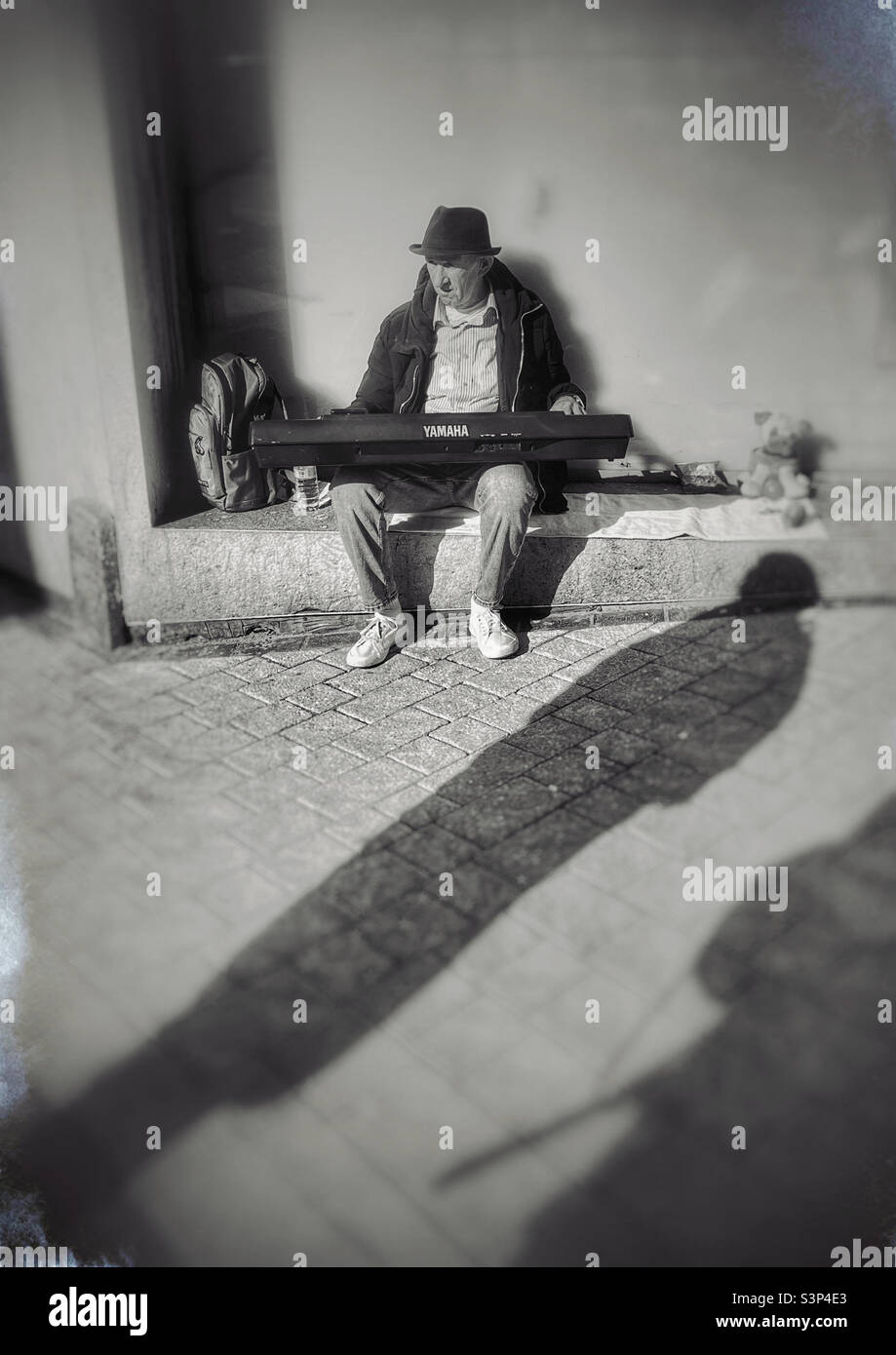 Busker playing Yamaha organ, as passerby casts long shadow close by - Smartphone Captured Stock Image
