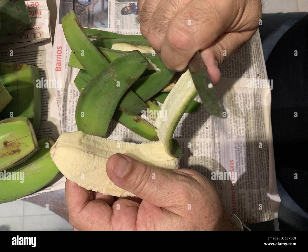 Human hands peeling off the skin of a plantain. Granma newspaper used to collect the peels. Havana, Cuba. - Smartphone Captured Stock Image