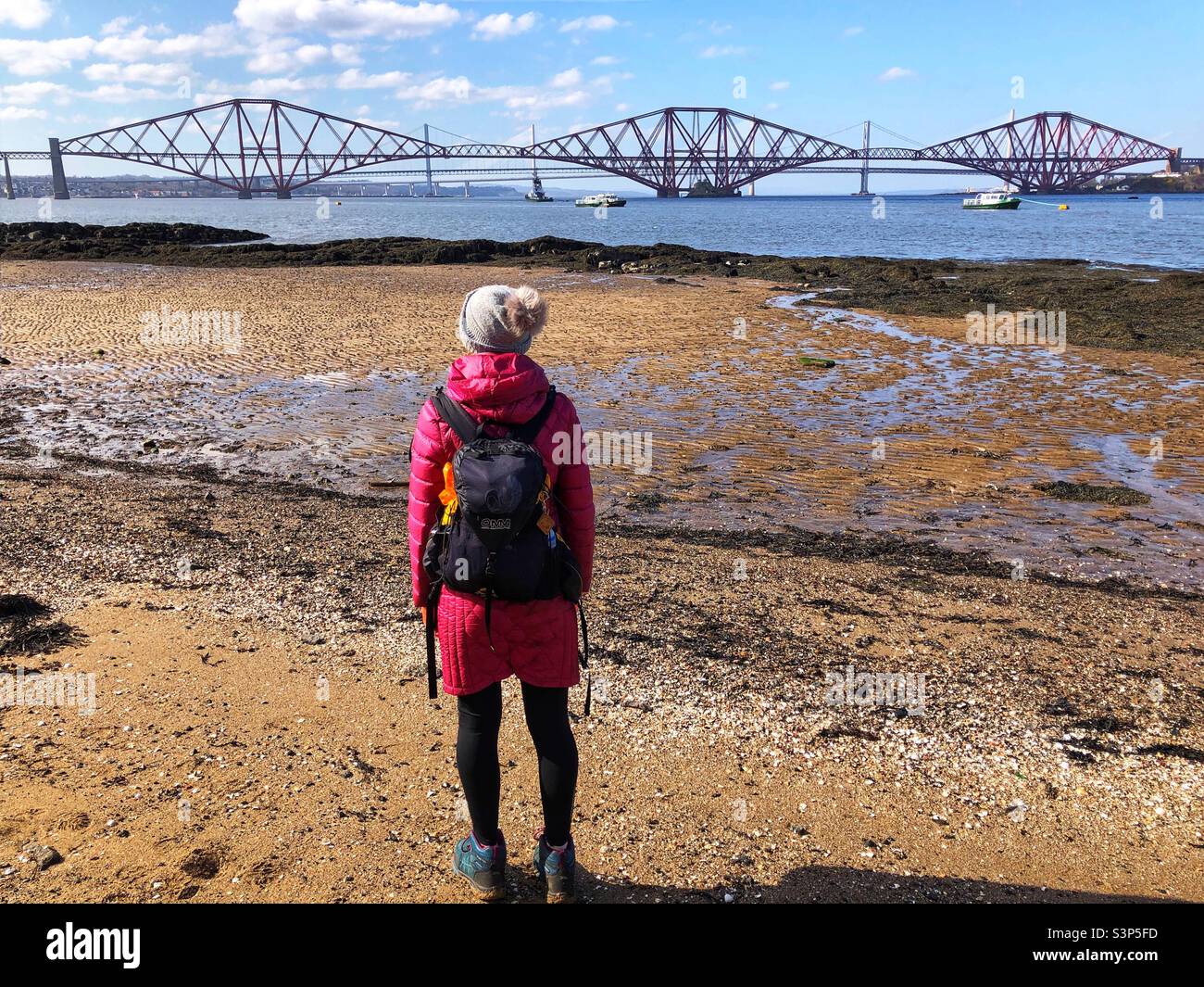 Woman hiker on the beach at the Firth of Forth estuary at low tide with a view of the Forth bridge, Scotland - Smartphone Captured Stock Image
