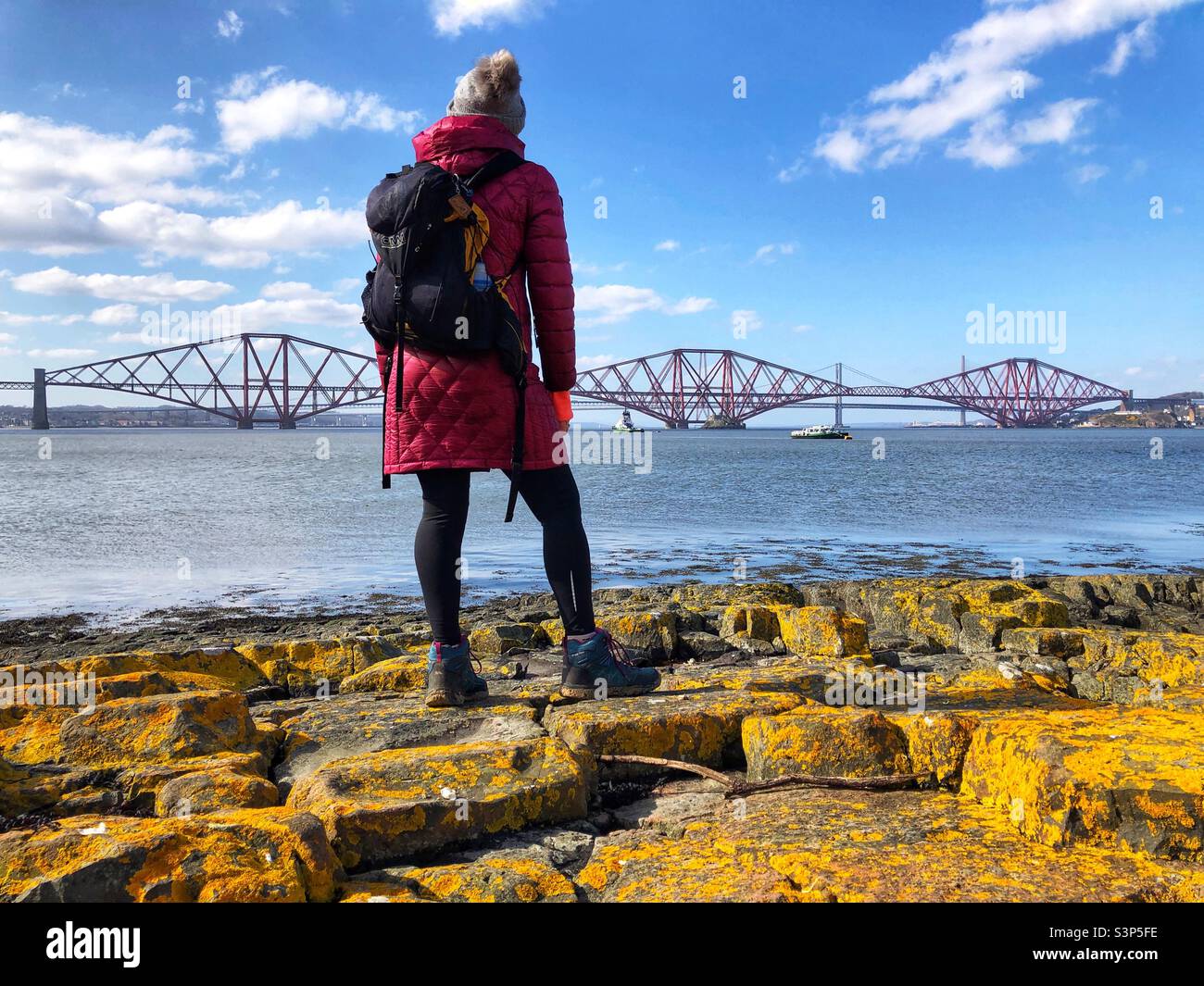 Woman hiker on the beach at the Firth of Forth estuary at low tide with a view of the Forth bridge, Scotland Stock Photo