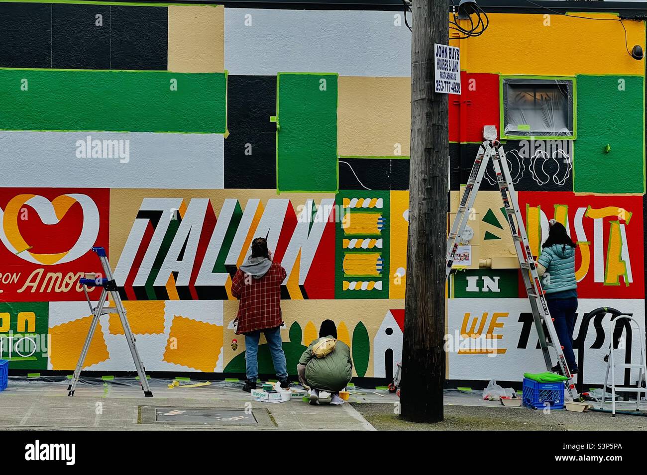 Repainting the facade outside an Italian Restaurant in Seattle’s Roosevelt Neighbourhood on a recent afternoon in bright colours on an overcast day. - Smartphone Captured Stock Image
