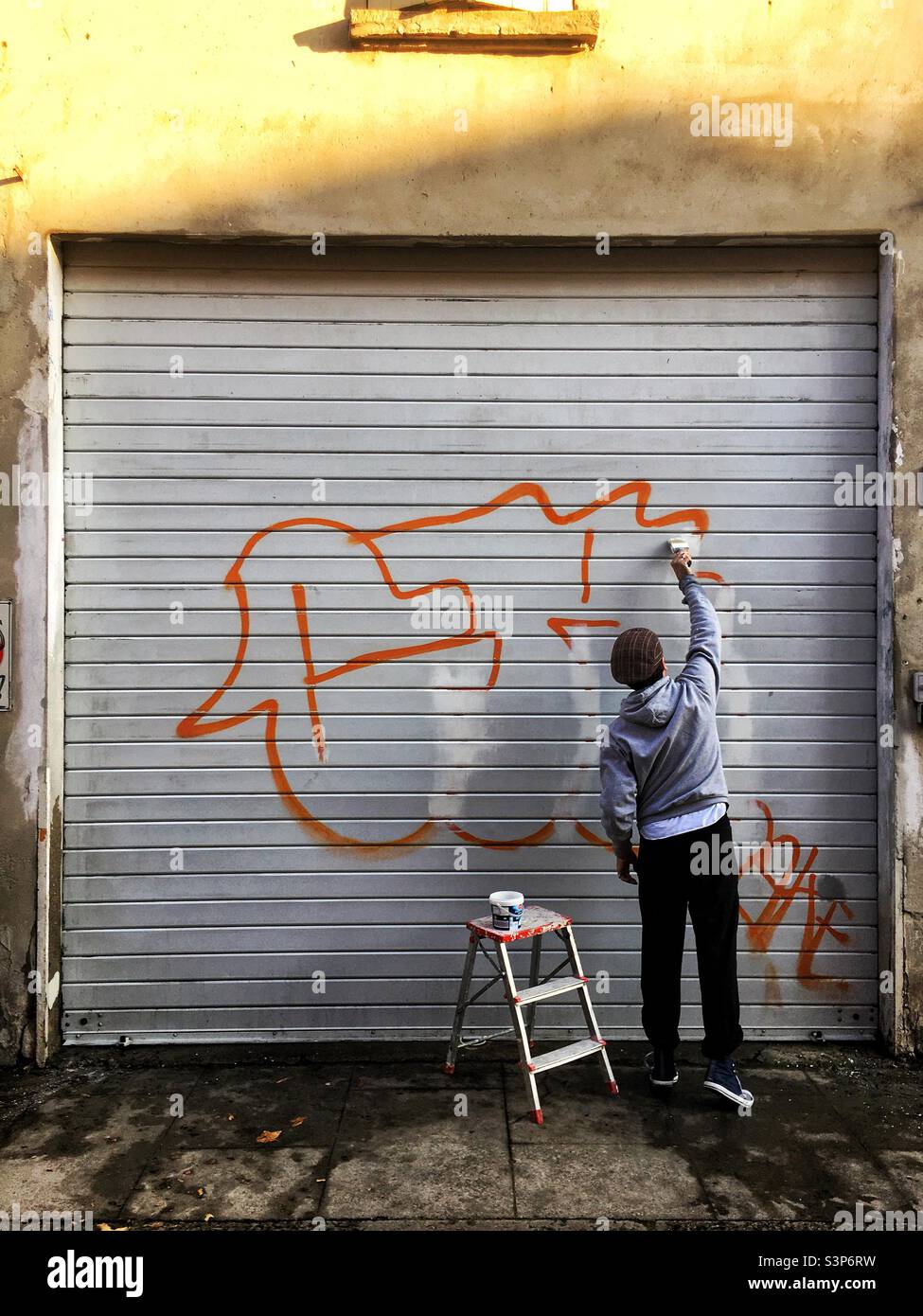 Man is cleaning a garage door from a graffiti. Stock Photo