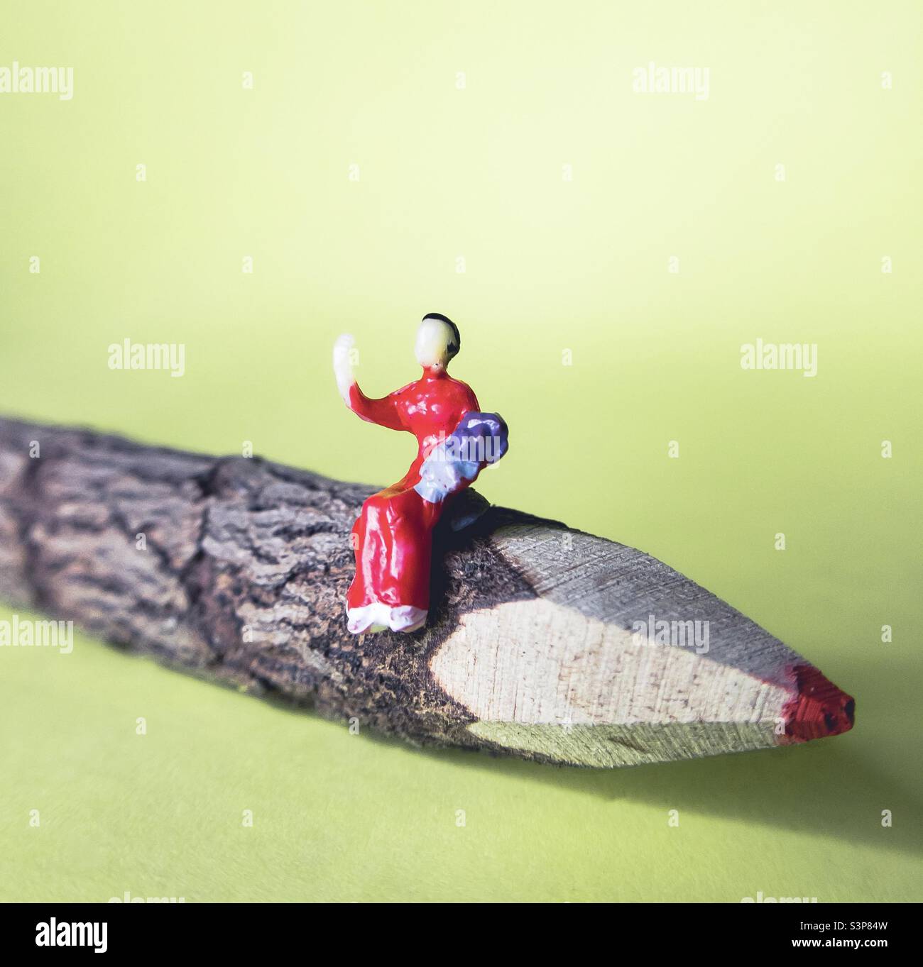 A model person holding a baby, waves to us from her seat atop of a red twig pencil against a yellow background - Smartphone Captured Stock Image