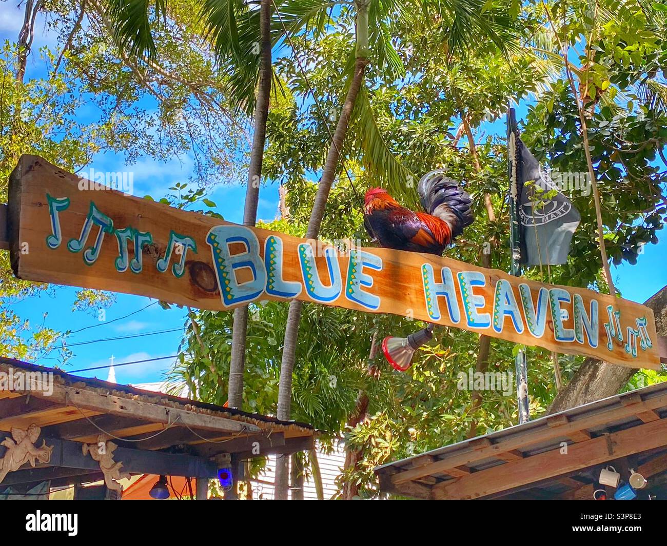 Rooster sitting on the sign of the Restaurant Blue Heaven Stock Photo
