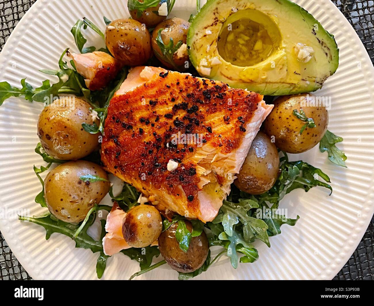 Flat lay of  a gourmet seafood meal of grilled salmon on a bed of arugula and new potatoes with accompanying avocado - Smartphone Captured Stock Image