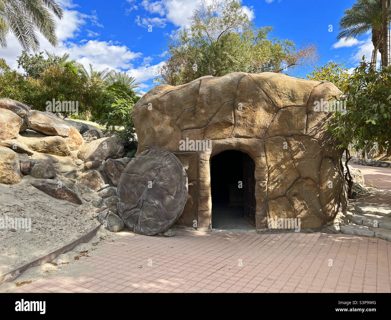Replica of the empty tomb of Jesus Christ with paved ground copy space and bright blue sky with trees in the background. - Smartphone Captured Stock Image
