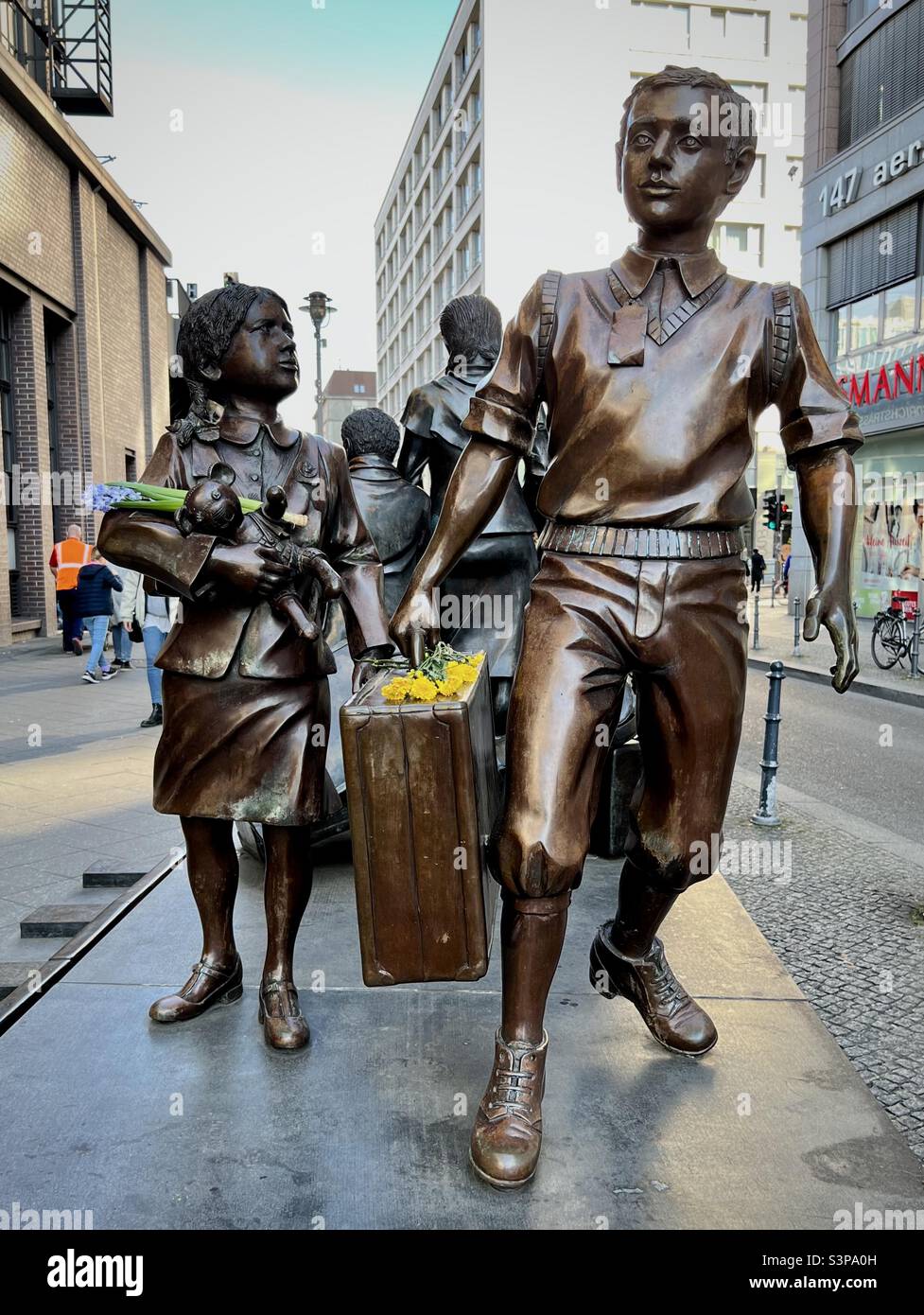 Germany, Berlin. 27 March 2022. Yellow and blue flowers remember plight of Ukrainian children during the Russian military invasion. (Sculpture - Kindertransport by Frank Meisler) - Smartphone Captured Stock Image