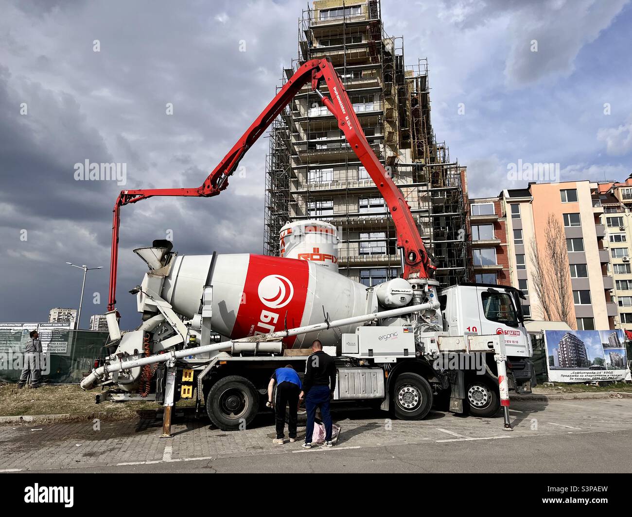 Red concrete pump truck by a new residential building construction site in Sofia, Bulgaria, Eastern Europe, Balkans - Smartphone Captured Stock Image
