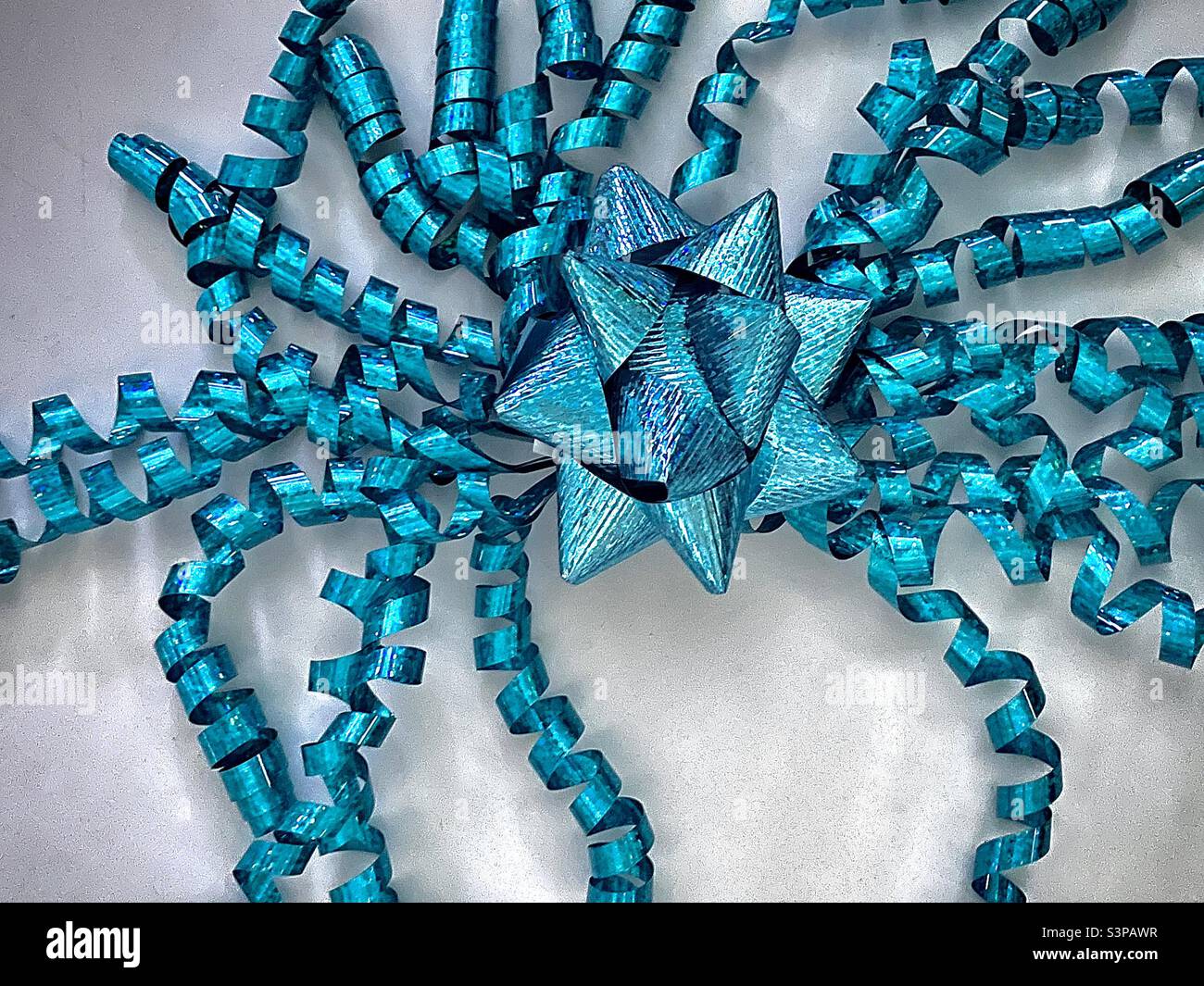 A turquoise gift bow and dangling curled ribbons photographed from above on a white background. - Smartphone Captured Stock Image