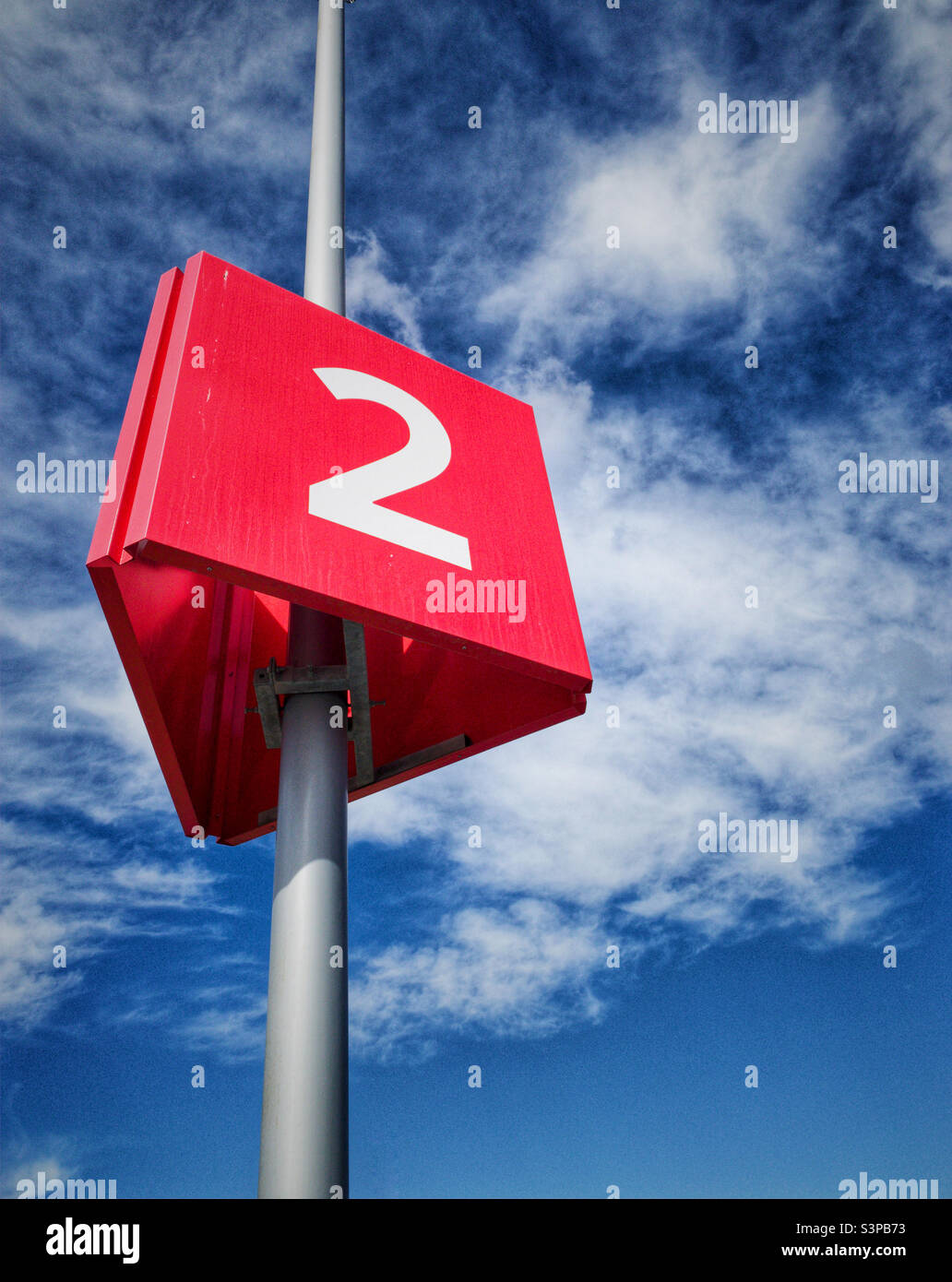 Number two white numeral on bright red triangular shaped sign hanging on a tall post with against a brilliant blue sky. - Smartphone Captured Stock Image