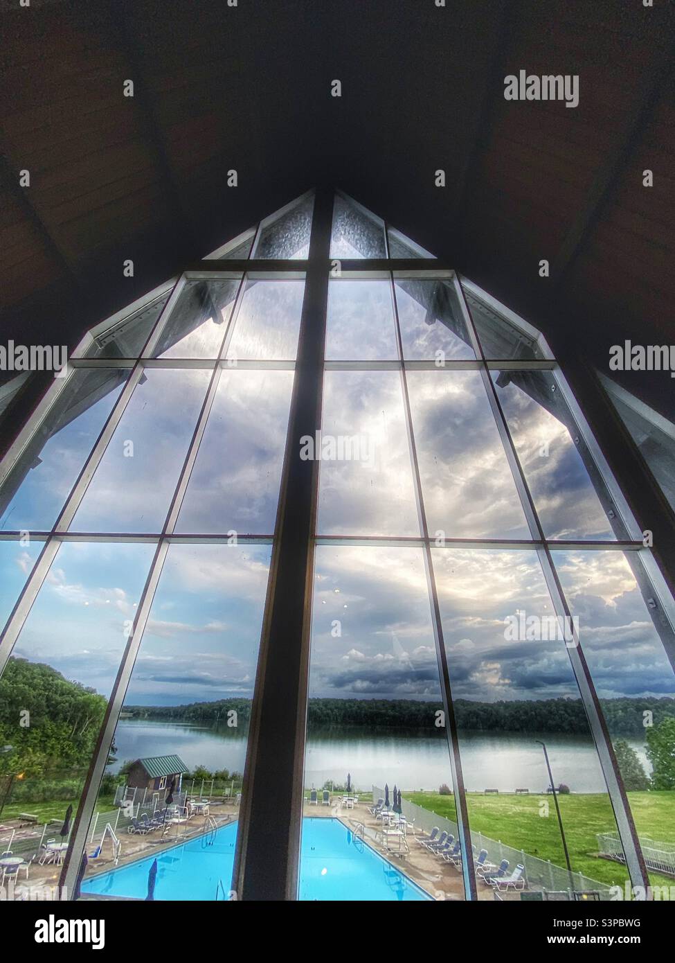 The view through a large window at Houston Woods Lodge.  A blue swimming pool, lake and trees can be seen. - Smartphone Captured Stock Image